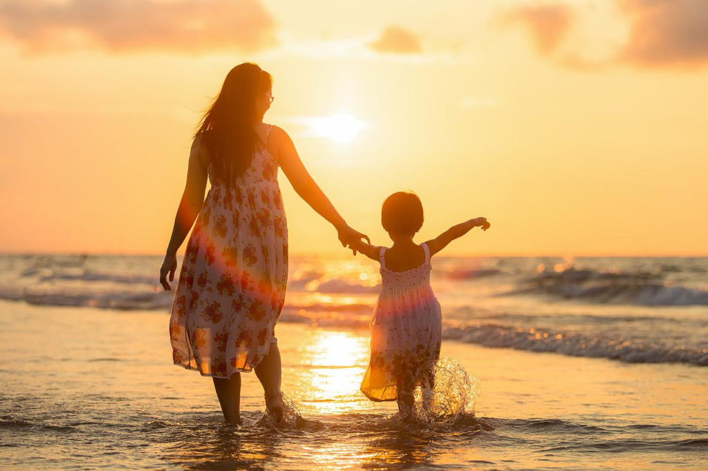 Mãe e filha caminhando juntas na beira do mar durante o por do sol e aprendendo como falar sobre família em inglês.
