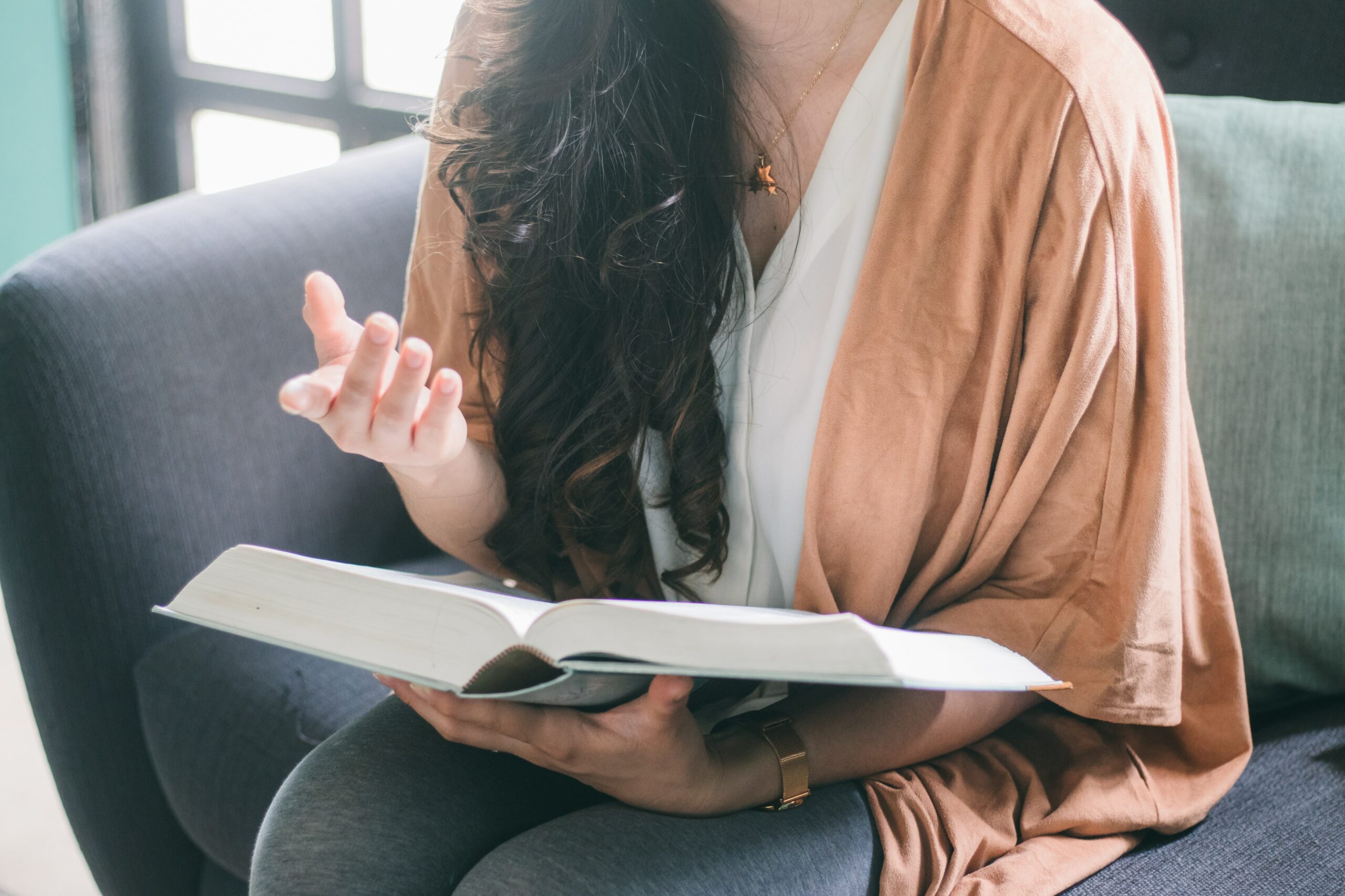 Mulher com um livro no colo treinando sua fala depois de aprender como melhorar a pronúncia em inglês.