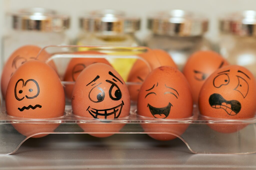 Foto de caixa de ovos em que cada ovo tem uma expressão rabiscada, representando que competências comportamentais não significam não expressar emoções.